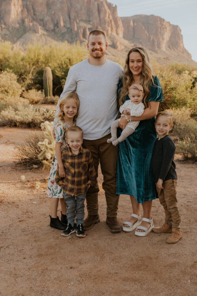 Parents with their four little kids all smile at the camera for pictures at Lost Dutchman State Park outside of Phoenix Arizona. #Arizonfamilyphotographer #Phoenixphotolocations #superstitionmountains #familyphotographer #ChelseyMichellePhotography #Scottsdalephotographer #familyphotosinspo #LostDutchmanStatePark