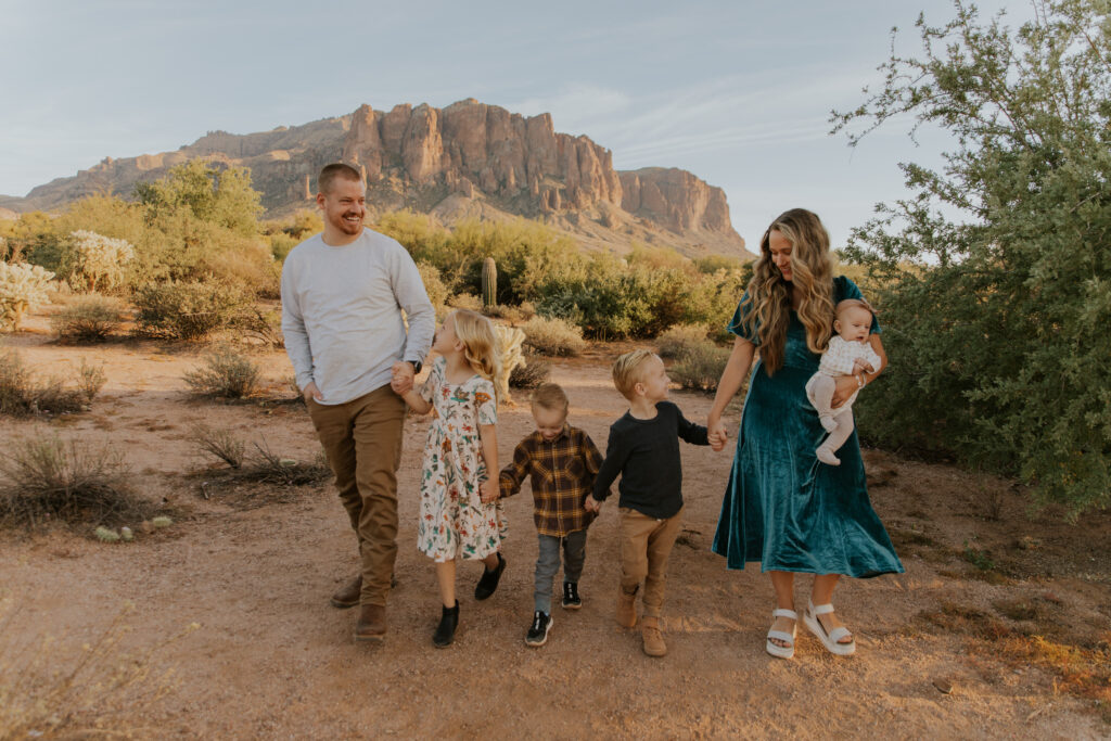 A candid photo of parents and their four little kids walking together in the desert of the Superstition Mountains. #Arizonfamilyphotographer #Phoenixphotolocations #superstitionmountains #familyphotographer #ChelseyMichellePhotography #Scottsdalephotographer #familyphotosinspo #LostDutchmanStatePark