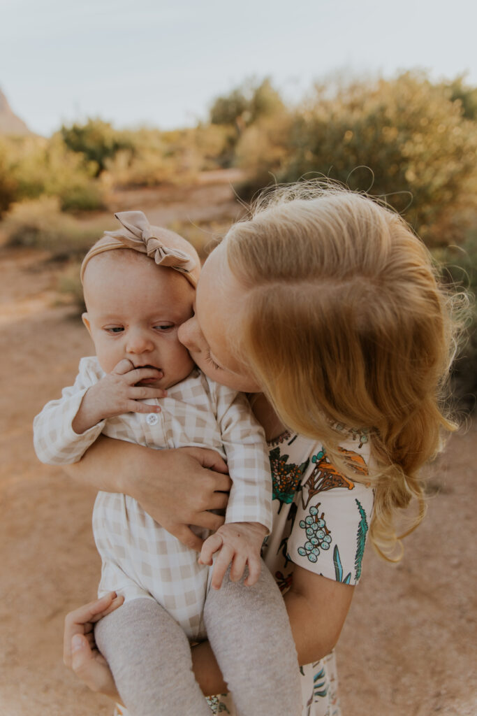 A memorable moment between sisters as the older one kisses her baby sibling on the cheek. #Arizonfamilyphotographer #Phoenixphotolocations #superstitionmountains #familyphotographer #ChelseyMichellePhotography #Scottsdalephotographer #familyphotosinspo #LostDutchmanStatePark