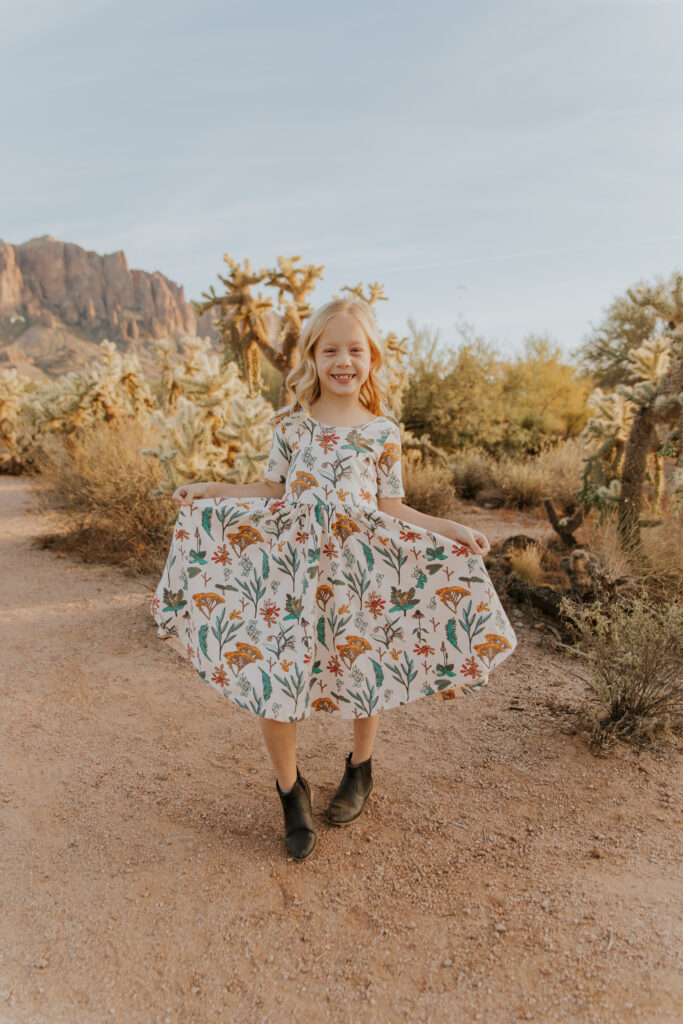 Adorable individual photo of a young girl holding her floral dress out to her sides and showing it off. #Arizonfamilyphotographer #Phoenixphotolocations #superstitionmountains #familyphotographer #ChelseyMichellePhotography #Scottsdalephotographer #familyphotosinspo #LostDutchmanStatePark