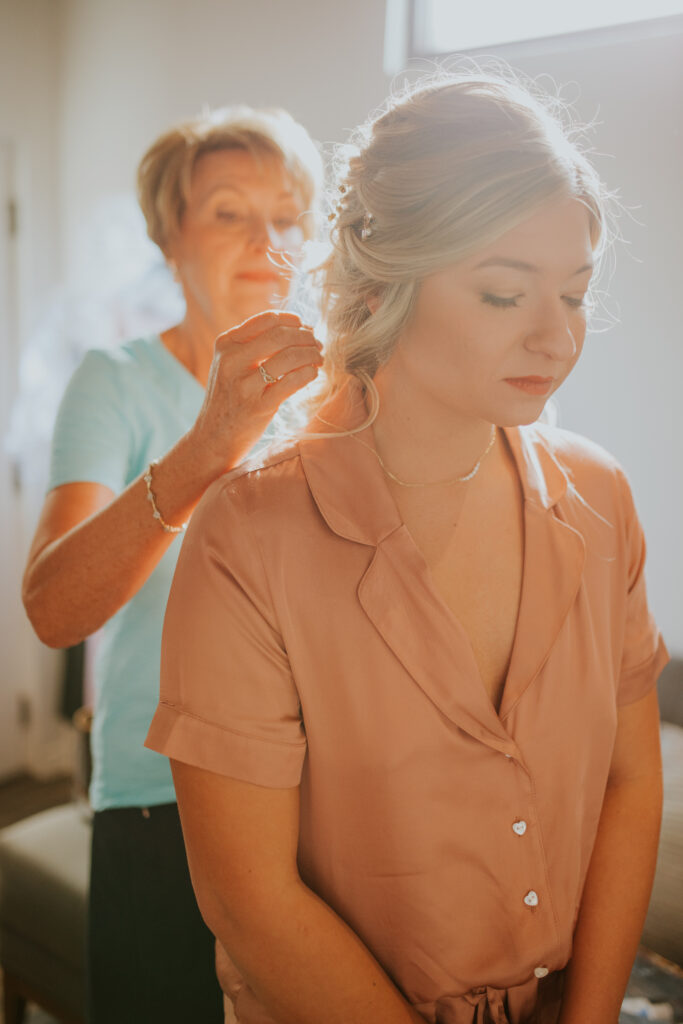 The mother of the bride helps her daughter with last-minute hair adjustments before her desert wedding. #ChelseyMichelleCoPhotography #Arizonaweddingphotographer #Phoenixweddingphotographer #Apachejunctionwedding #ThePaseo #weddingatThePaseo #Gilbertphotographer #Arizonadestinationwedding