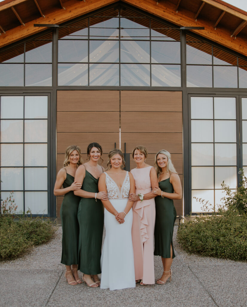 Bride and bridal party smile together wearing white, forest green, and blush pink dresses at The Paseo. #ChelseyMichelleCoPhotography #Arizonaweddingphotographer #Phoenixweddingphotographer #Apachejunctionwedding #ThePaseo #weddingatThePaseo #Gilbertphotographer #Arizonadestinationwedding