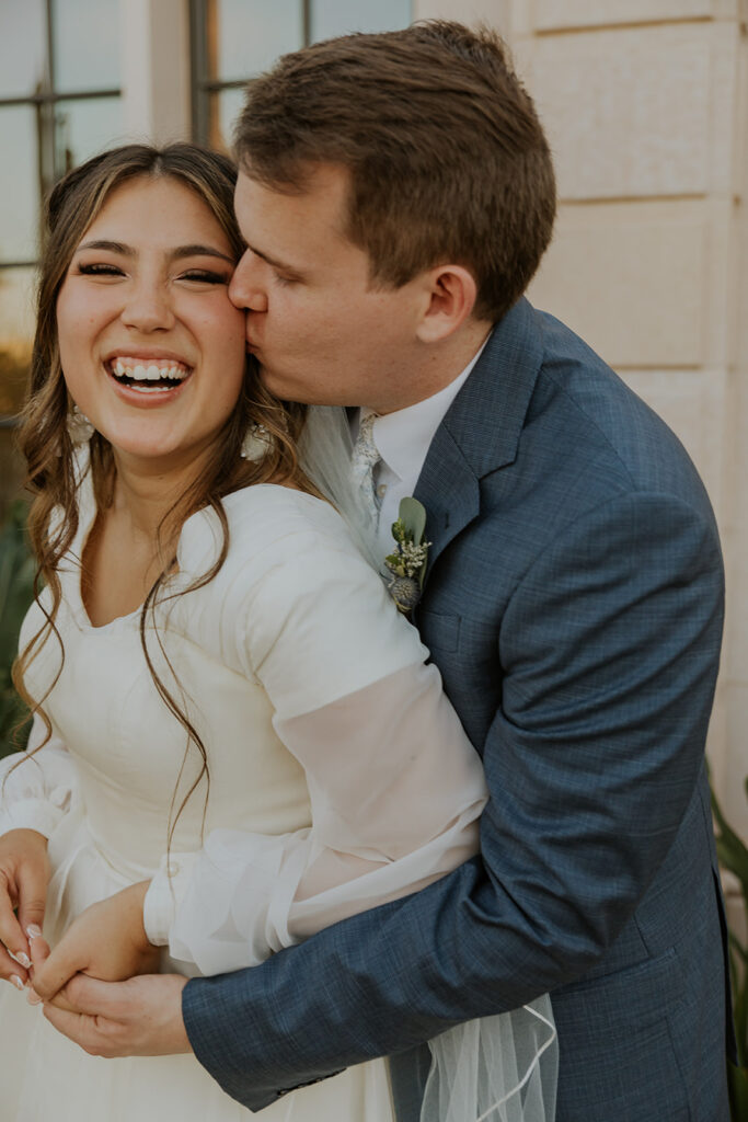 Romantic candid wedding photo of groom hugging smiling bride at Mesa Arizona temple during golden hour, photo by Chelsey Michelle. #ChelseyMichelleCoPhotography #Arizonaweddingphotographer #Phoenixphotographer #Mesaphotographer #Gilbertphotographer #ArizonaLDSwedding