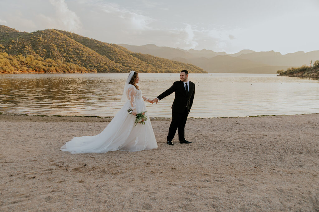 Bride and groom walk hand in hand on the edge of a lake. Groom walks a bit ahead and looks back so lovingly at his bride.
#ChelseyMichelleCoPhotography #ArizonaWeddingPhotographer #PhoenixPhotographer #MesaPhotographer #BridalPhotos #SaguroLake
