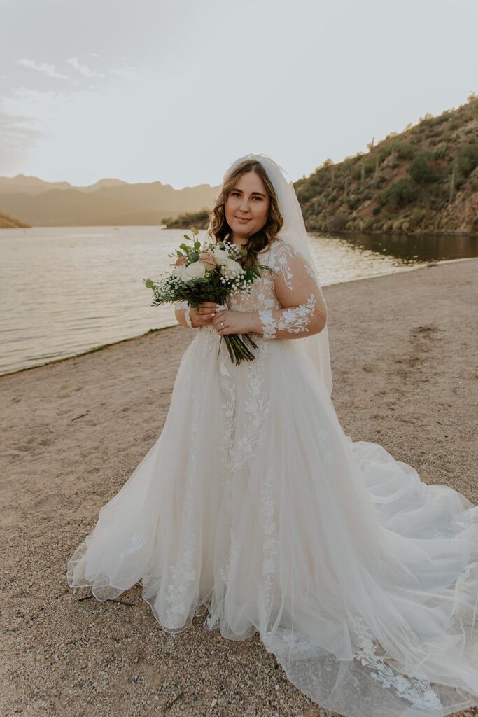 Standing in front of a gorgeous lake view, a bride smiles sweetly at Chelsey Michelle Co Photography. Arizona based bridal photo session.
#ChelseyMichelleCoPhotography #ArizonaWeddingPhotographer #PhoenixPhotographer #MesaPhotographer #BridalPhotos #SaguroLake
