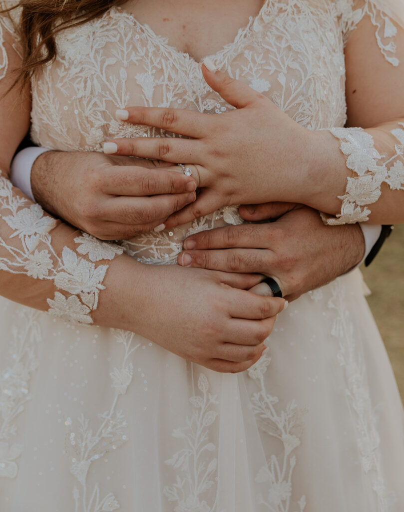 Groom places his arms gently around his bride. Both bride and groom display their wedding rings.
#ChelseyMichelleCoPhotography #ArizonaWeddingPhotographer #PhoenixPhotographer #MesaPhotographer #BridalPhotos #SaguroLake
