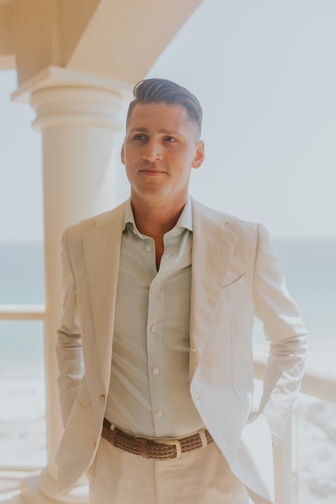 A dashing groom stands near a balcony’s edge with his hands in his back pockets. Chelsey Michelle Co Photography captures all of the important people at a Florida destination wedding. #DestinationWedding #ChelseyMichelleCoPhotography #SummerWedding #FloridaWedding