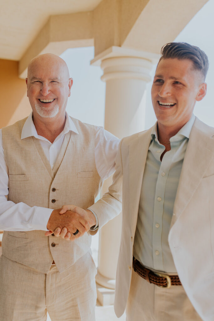 Chelsey Michelle Co Photography photographs a groom who shares a joyful moment with his father in law on the day of his wedding. Light colored suits. Happy family moments. #DestinationWedding #ChelseyMichelleCoPhotography #SummerWedding #WeddingOnTheBeach #FloridaWedding
