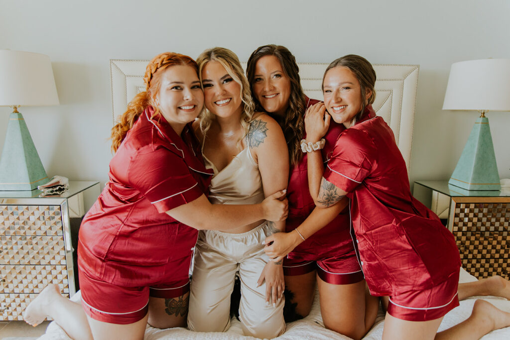 A darling bride kneels on a bed with her three bridesmaids kneeling by her side. The women are in fun summer pajama sets. Destination wedding captured by Chelsey Michelle Co Photography.
#DestinationWedding #ChelseyMichelleCoPhotography #SummerWedding #FloridaWedding