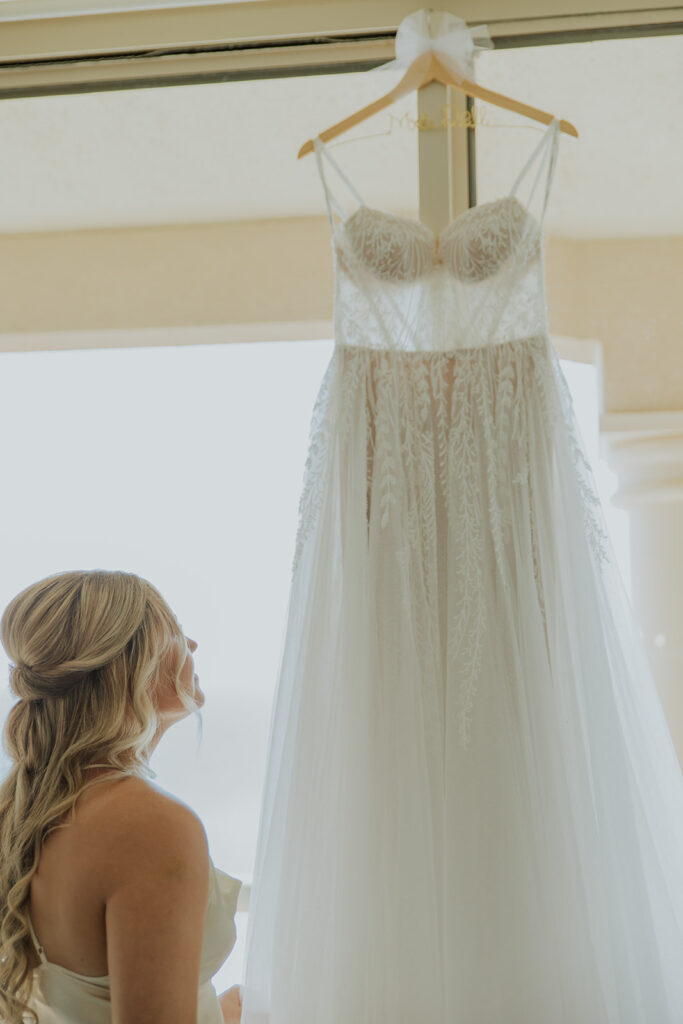 The most beautiful bride stares up adoringly at her wedding dress on a hanger. Chelsey Michelle Co Photography captures big and small moments during the wedding day. #DestinationWedding #ChelseyMichelleCoPhotography #SummerWedding
#WeddingPrep #FloridaWedding
