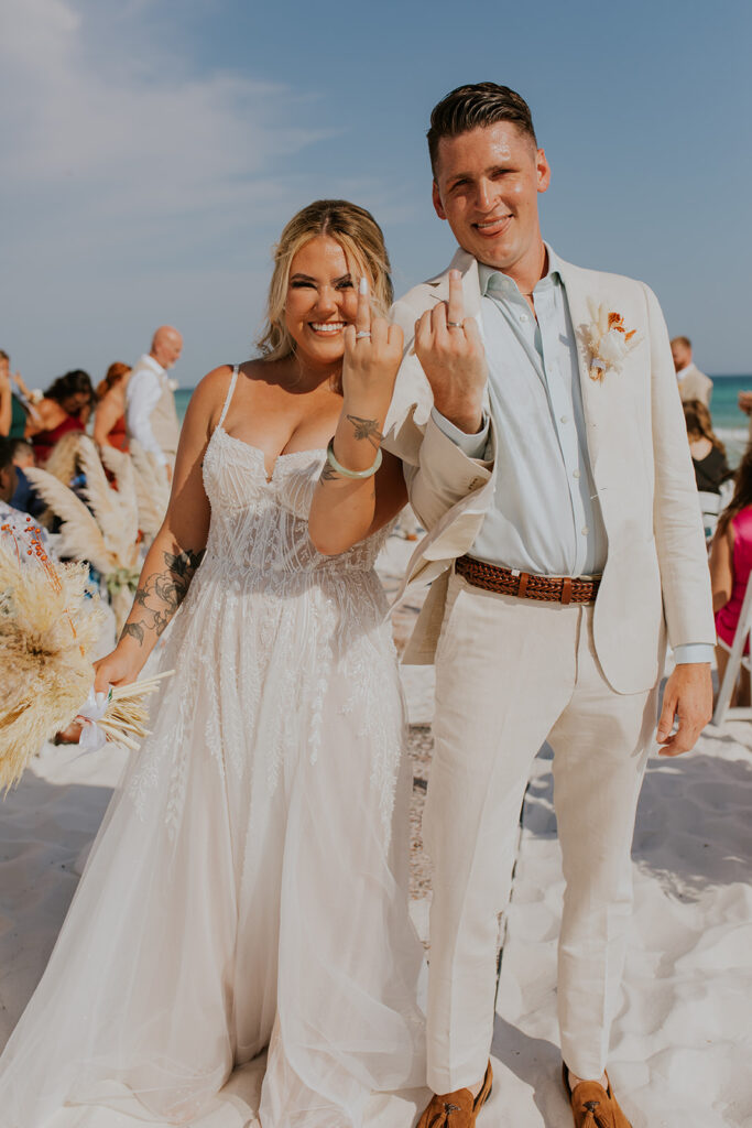 Bride and groom share a lighthearted moment displaying their wedding rings by holding up their ring fingers. Chelsey Michelle Co Photography captures fun, small, memorable moments on wedding day. #DestinationWedding #ChelseyMichelleCoPhotography #SummerWedding #FloridaWedding
