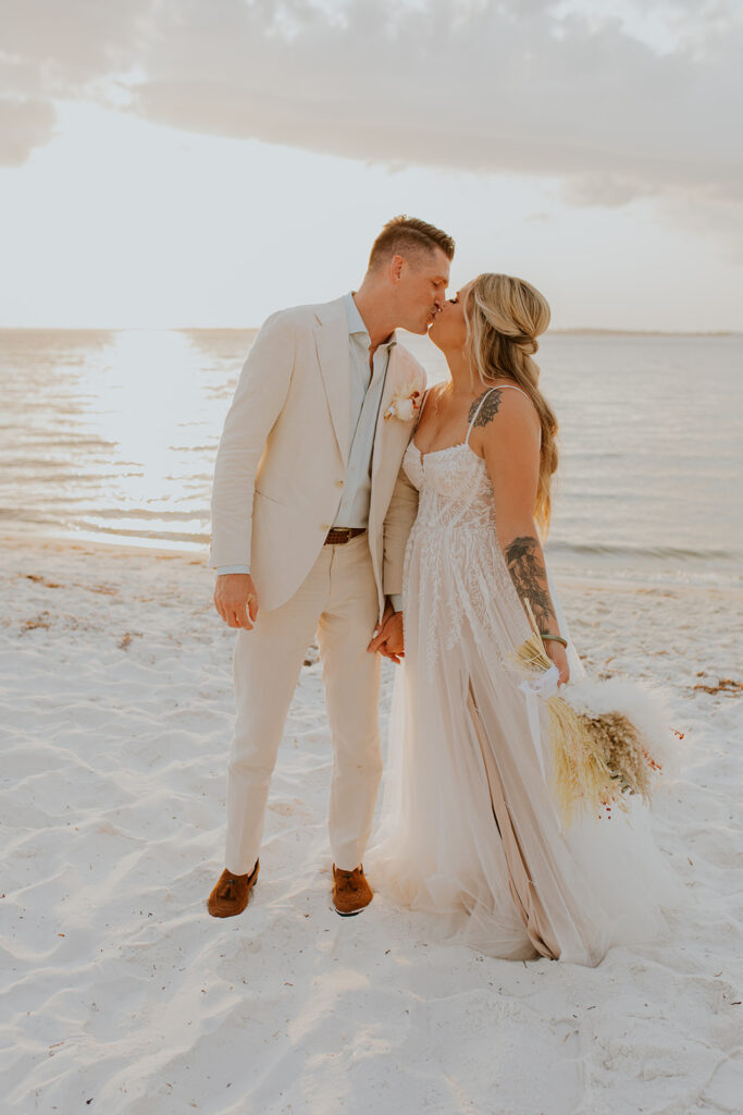 A happy bride and groom are captured by Chelsey Michelle Co Photography on the beach near the ocean’s edge as the sun begins to set. They share a sweet kiss. Florida wedding details. #DestinationWedding #ChelseyMichelleCoPhotography #SummerWedding #FloridaWedding
