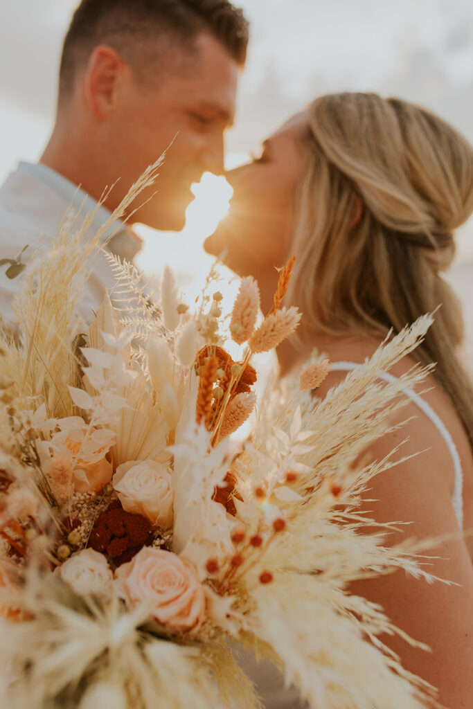 A close up image of a beautiful bridal bouquet with the bride and groom in the background standing nose to nose. Wedding at Pensacola Beach captured by Chelsey Michelle Co Photography. Wedding bouquet #DestinationWedding #ChelseyMichelleCoPhotography #SummerWedding #FloridaWedding
