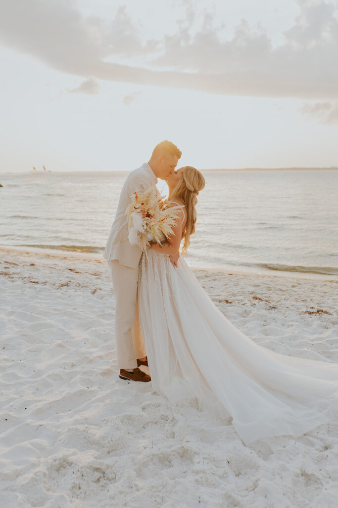 Chelsey Michelle Co Photography captures a stunning image of a bride and groom standing on the beach kissing at sunset. Romantic wedding day pictures. Florida wedding. #DestinationWedding #ChelseyMichelleCoPhotography #SummerWedding #FloridaWedding