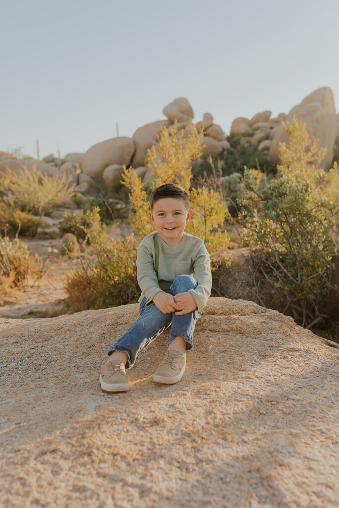 A sweet young boy sits on top of a large rock while folding his arms over his knees during an East Valley Arizona photoshoot. He grins widely at Chelsey Michelle Co Photography. Arizona family photographer.
#ChelseyMichelleCoPhotography #MaternityPhotos #EastValleyAZ #familyphotos
