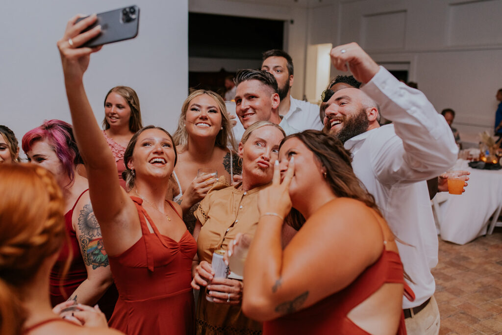 A photo of a bride and groom posing for a selfie with two bridesmaids and a few other wedding guests. Happy friends at a wedding reception in Florida. Chelsey Michelle Co Photography is great at capturing candid moments. #DestinationWedding #ChelseyMichelleCoPhotography #SummerWedding #FloridaWedding
