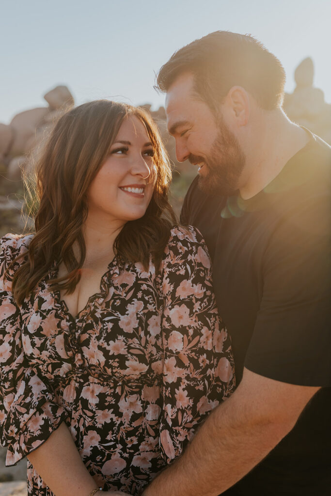 The most darling couple grin at each other during a family and maternity photo session in Phoenix Arizona. Woman in fashionable floral dress. Maternity sessions with Chelsey Michelle Co Photography.
#ChelseyMichelleCoPhotography #MaternityPhotos #EastValleyAZ #familyphotos
