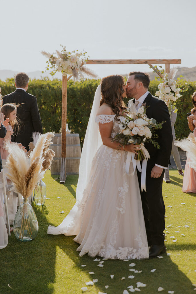 A couple kisses as they walk back down the aisle after becoming husband and wife, surrounded in desert green and beautiful natural sunlight. Florals fairy tale I do wedding ceremony brides bouquet rose petals design #Desertweddingvenues #ArizonaWeddingVenue #Arizonaweddingphotographer #Mesaweddingphotographer

