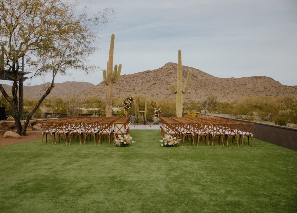 A stunning wedding ceremony location with the perfect cactus towering around and creating the desert vibes of your dreams. Wooden chairs circle floral archway desert mountains grass wedding ceremony #Desertweddingvenues #ArizonaWeddingVenue #Arizonaweddingphotographer #Mesaweddingphotographer



